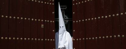 Un nazareno de La Paz junto a la cruz guía abre la puerta del templo para iniciar la estación de penitencia de su Hermandad, en la jornada en la que comienzan los desfiles procesionales del Domingo de Ramos, en Sevilla.