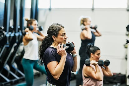 Una mujer hace sentadillas con mancuernas durante la clase de 'fitness' en el gimnasio.