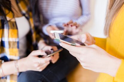 Tres chicas manejan sus teléfonos móviles.