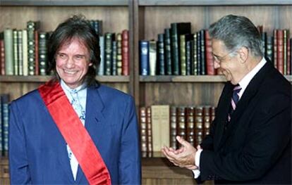 Roberto Carlos, con corbata y banda de la Orden del Mérito Cultural, sonríe ante el presidente brasileño.