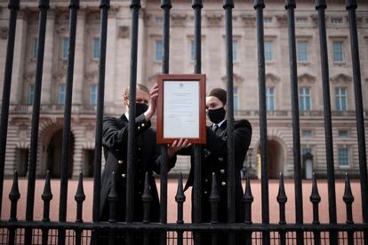 Dos miembros del personal de Buckinghman colocan el anuncio del fallecimiento del príncipe Felipe en la entrada del palacio.