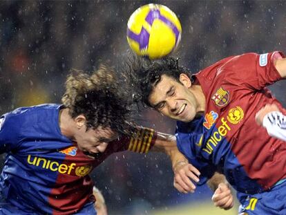 Puyol y Márquez saltan a la vez para intentar despejar de su área el balón.