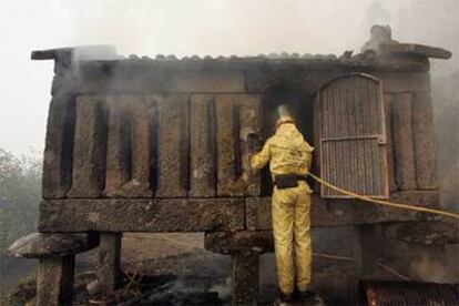 Un bombero intenta sofocar las llamas dentro de un hórreo en Cotobade (Pontevedra).