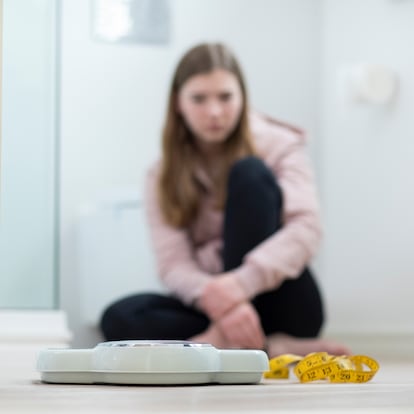 Unhappy Teenage Girl Sitting In Bathroom Looking At Scales And Tape Measure