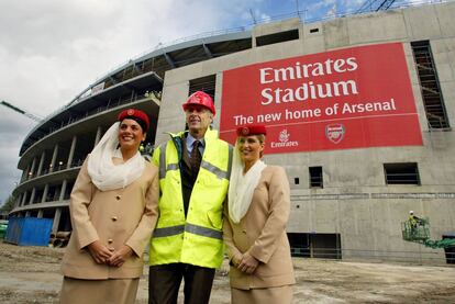 Arsene Wenger posa con dos azafatas de Emirates Airlines frente al nuevo estadio del Arsenal en Londres, el 5 de octubre de 2004. 