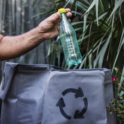 Man's hand throwing away a plastic water bottle into a recycling bag: sustainable lifestyle