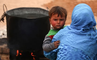 A displaced Syrian child, who fled the countryside surrounding the Islamic State (IS) group stronghold of Raqa, looks on as he is being held by a woman at a temporary camp in the village of Ain Issa on April 28, 2017. / AFP PHOTO / DELIL SOULEIMAN