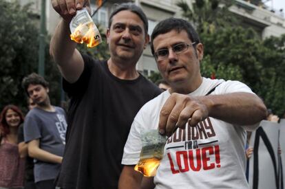 Dos hombres queman billetes de cinco euros en Atenas el pasado 28 de junio de 2015 durante una protesta ciudadana por el corralito impuesto por el Gobierno heleno tras secarse la financiación que recibía Grecia desde el Banco Central Europeo. Se impuso una restricción muy fuerte a la retirada de efectivo de los bancos, limitada a 60 euros diarios por persona. | <a href=http://internacional.elpais.com/internacional/2015/06/28/actualidad/1435511187_526473.html target=”blank”>IR A LA NOTICIA</a>