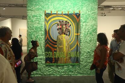 Personas miran el arte textil de April Bey, originaria de Bahamas, titulado 'They Still Glorify Labor and Toxic Resilience but Can't Even Duplicate Their Limbs' (2023), en Miami.