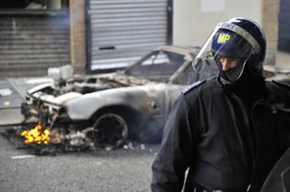 Un policía antidisturbio, frente a un vehículo quemado en Hackney, al este de Londres, durante el tercer día de disturbios.