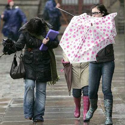 Unas jóvenes intentan caminar entre el fuerte viento y la lluvia en una calle de Santiago de Compostela.