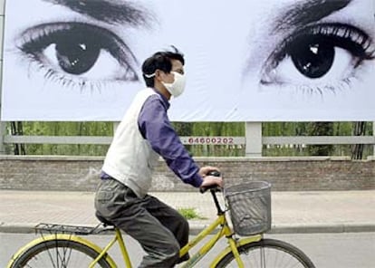Un ciudadano con mascarilla protectora circulaba ayer en bicicleta ante una valla publicitaria en Pekín.
