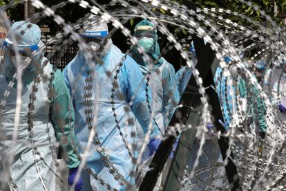 Personal sanitario protegido con trajes y mascarillas cruza una zona protegida, en Petaling Jaya (Malasia).