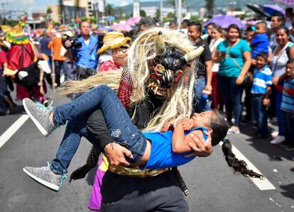 Un juerguista disfrazado de personaje mitológico sostiene a una niña durante un desfile que marca el inicio de la fiesta del santo patrón de San Salvador en honor a Divino Salvador del Mundo, en San Salvador.