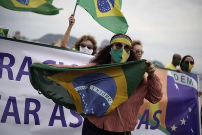 Seguidora de Jair Bolsonaro usa máscara verde-amarela e carrega a bandeira do Brasil em ato a favor do presidente na praia de Copacabana, no Rio de Janeiro.