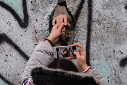 Um visitante passa a mão por um buraco na parede para tirar uma foto.