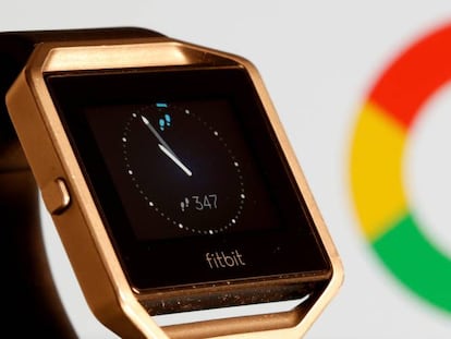 Reloj de la compañía Fitbit frente a una pantalla con el logotipo de Google.