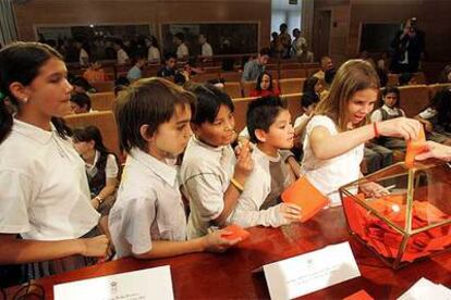 Varios escolares depositan sus votos en una urna en la jornada infantil <i>Diputados por un día</i>, celebrada en la Asamblea de Madrid.