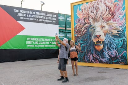 Tres asistentes se sacan un 'selfie' frente a un mural en el festival Rototom Sunsplash, en Benicàssim (Castellón). A un lado, la bandera de Palestina.