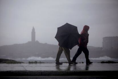 Dos hombres caminaban hoy por el paseo marítimo de A Coruña, con la Torre de Hércules al fondo.