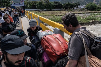Venezolanos cruzan con maletas por el puente Simón Bolívar, mientras la prensa espera el acto oficial.