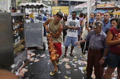 Um ambulante vende frango assado ao lado de fila de eleitores, que aguardam para votar no Complexo do Alemão, no Rio de Janeiro.