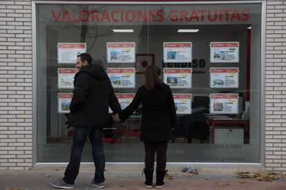 Dos jóvenes miran un escaparate con anuncios de pisos en el Ensanche de Vallecas (Madrid).