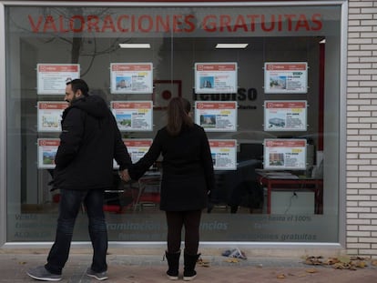 Dos jóvenes miran un escaparate con anuncios de pisos en el Ensanche de Vallecas (Madrid).