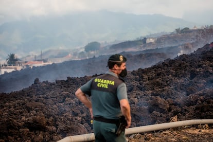 Un oficial de la Guardia Civil observa el humo que se eleva proveniente de la lava que fluyó sobre una carretera.