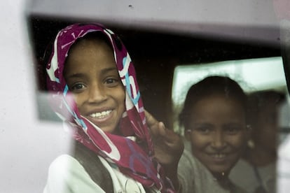 Una joven refugiada saharaui vestida con la típica melhfa, un lienzo de tela suave y con gran colorido con el que se cubren la cabeza y los hombros, sonríe desde el autobús que la llevará hasta su familia de acogida. En su mochila apenas llevan ropa y algún detalle como pulseras hechas por su familia para regalar como agradecimiento.
