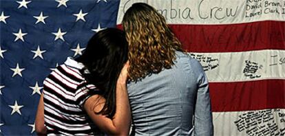 Dos adolescentes leen los mensajes escritos en una bandera por los asistentes a la ceremonia de homenaje a la tripulación del <i>Columbia</i> celebrada el martes en Houston.