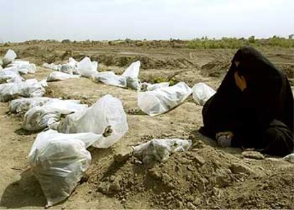 Una mujer llora sentada junto a decenas de bolsas con restos de víctimas de una matanza de chiíes ordenada por Sadam Husein en Mahawil.
