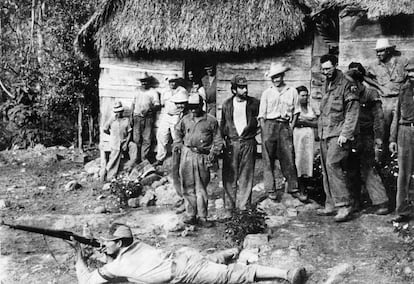 Fidel Castro, a la derecha de la imagen con gafas, contempla a un guerrillero mientras hace ejercicios de tiro tendido en el suelo, con varios guerrilleros más observando la escena, tomada en Sierra Maestra en fecha sin determinar.