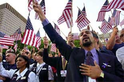 Un representante de American Airlines sostiene una bandera en alto con la mano en el corazón junto a otros norteamericanos en una plegaria en Boston.
