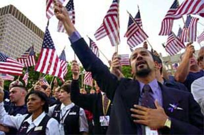 Un representante de American Airlines sostiene una bandera en alto con la mano en el corazón junto a otros norteamericanos en una plegaria en Boston.