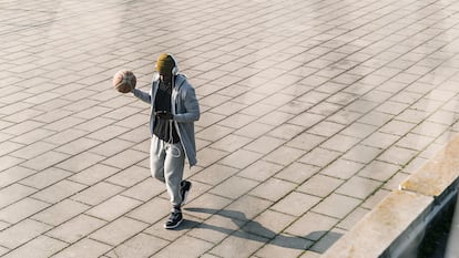 Un chico en chándal con su móvil y un balón de baloncesto por la calle.