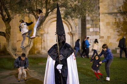Niños juegan junto a un penitente de la cofradía "Jesús en su Tercera Caída" durante la procesión en Zamora (España).