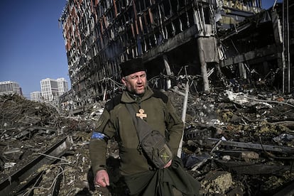 El capellán del ejército de Ucrania, Mikola Madenski, camina entre los escombros del centro comercial atacado este lunes, en Kiev. El ministro de Inclusión, Seguridad Social y Migraciones español, José Luis Escrivá, ha asegurado este lunes que unos 25.000 ucranios han llegado a España desde el inicio de la guerra hace casi un mes. A unos 9.000 ya se les ha concedido la protección temporal que les asegura permiso de residencia y trabajo.