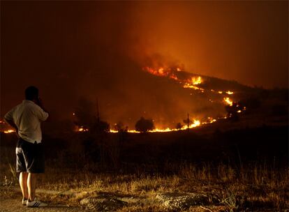 Un hombre habla por teléfono mientras observa como las llamas consumen una colina. Las autoridades locales creen que los incendios son provocados para poder edificar en las zonas calcinadas