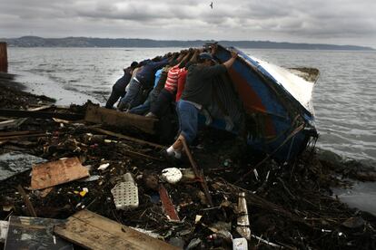 Pescadores voltean un bote que fue arrastrado a más de 16 kilómetros del puerto de Concepción y depositado en una playa junto con decenas de contenedores.