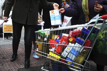 Una niña observa cómo su madre regala leche, luego de hacer la compra.