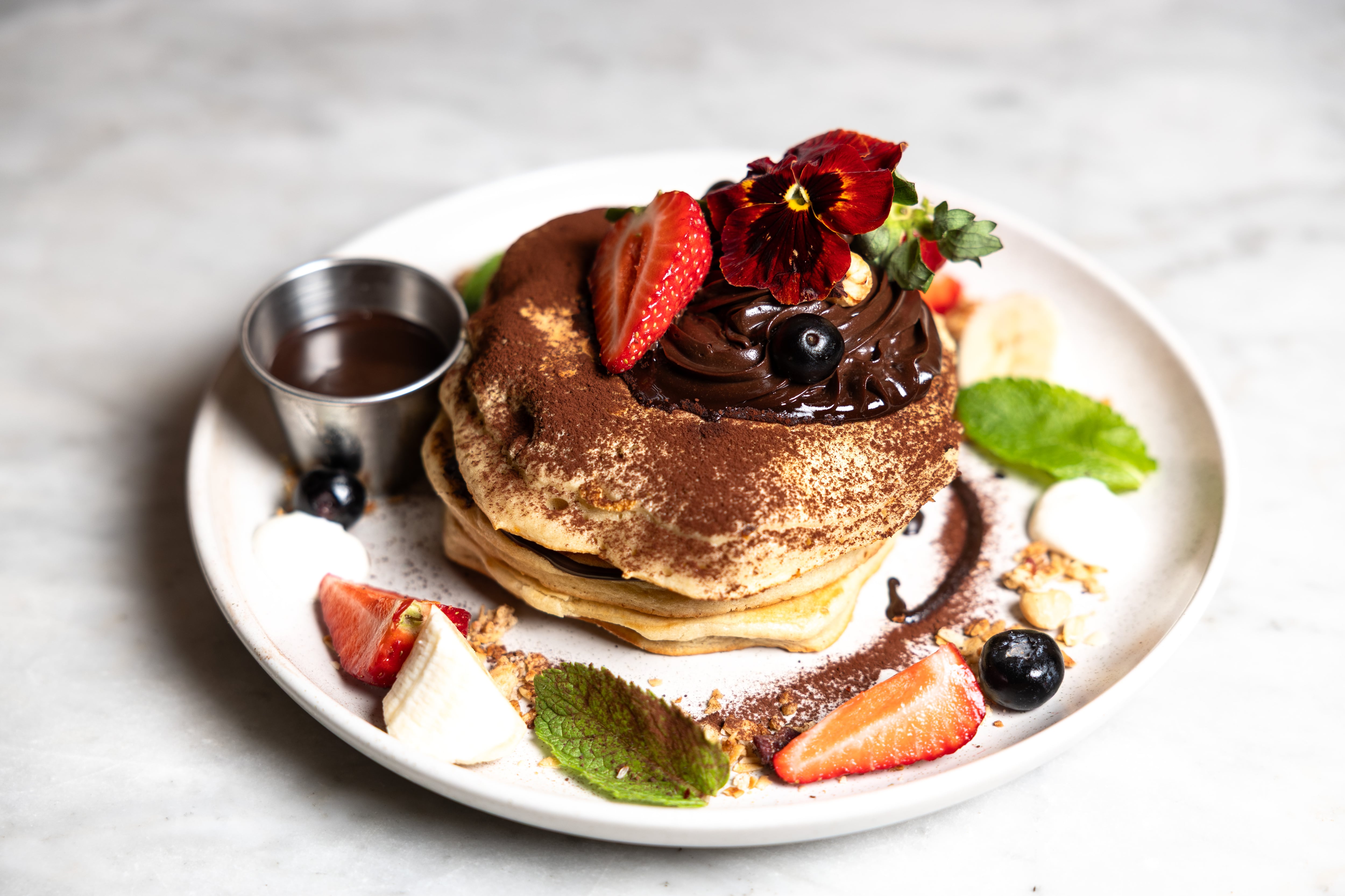 Tortitas con chocolate, arándanos, fresas y plátano, acompañadas de nata agria, granola y avellanas tostadas.