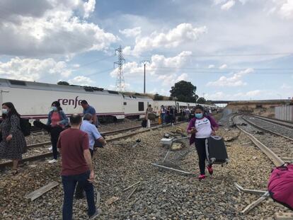 Varios pasajeros salen del tren descarrilado, con sus pertenencias.