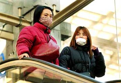 Dos mujeres, con mascarilla para protegerse de la epidemia, en la estación de trenes de Shanghai.