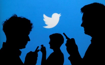 Tres personas consultan su teléfono móvil ante una pantalla de Twitter.