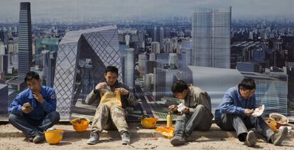 Varios obreros comen ante una imagen del distrito financiero de Pek&iacute;n.
