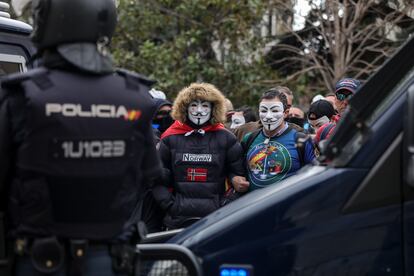 Un agente antidistrubios, frente a manifestantes con máscaras de Anonymous convocados por la asociación de policías y guardias civiles Jusapol