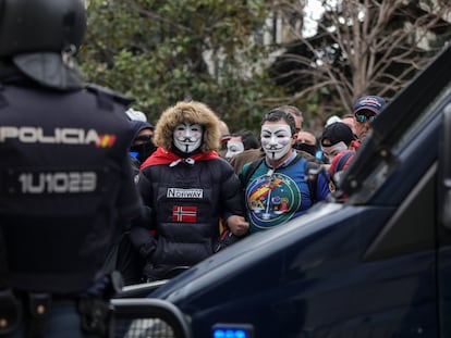 Un agente antidistrubios, frente a manifestantes con máscaras de Anonymous convocados por la asociación de policías y guardias civiles Jusapol