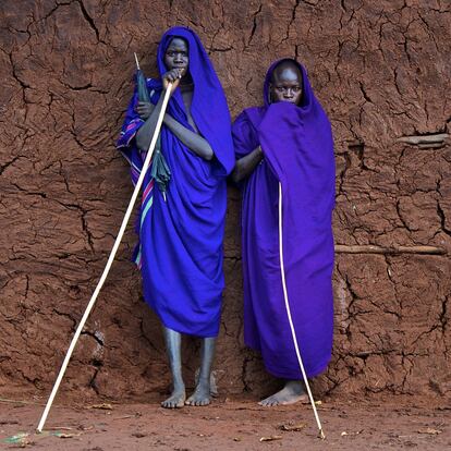 El vivo color azul de las togas de los jóvenes suris resalta ante el agrietado muro de adobe en en el valle del Omo, Etiopía. Suri, valle bajo del río Omo, Etiopía