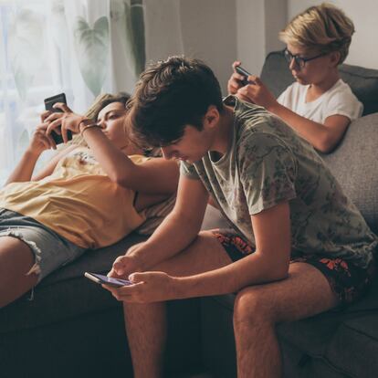 Group of teenager using smartphone sitting on a sofa at home. Young boys and a girl sharing photo and video watching social story online. Friends enjoying new trend technology. Youth and tech concept